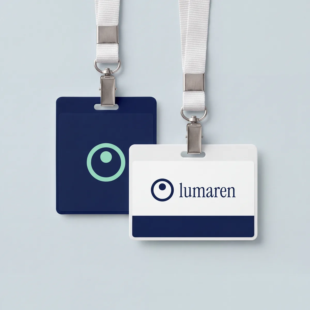 שני תגי צוות על שרוכים לבנים של מרפאת Lumaren הבדויה: תג כחול כהה עם סמל טבעת ונקודה במנטה, ותג לבן עם הסמל ושם המותג