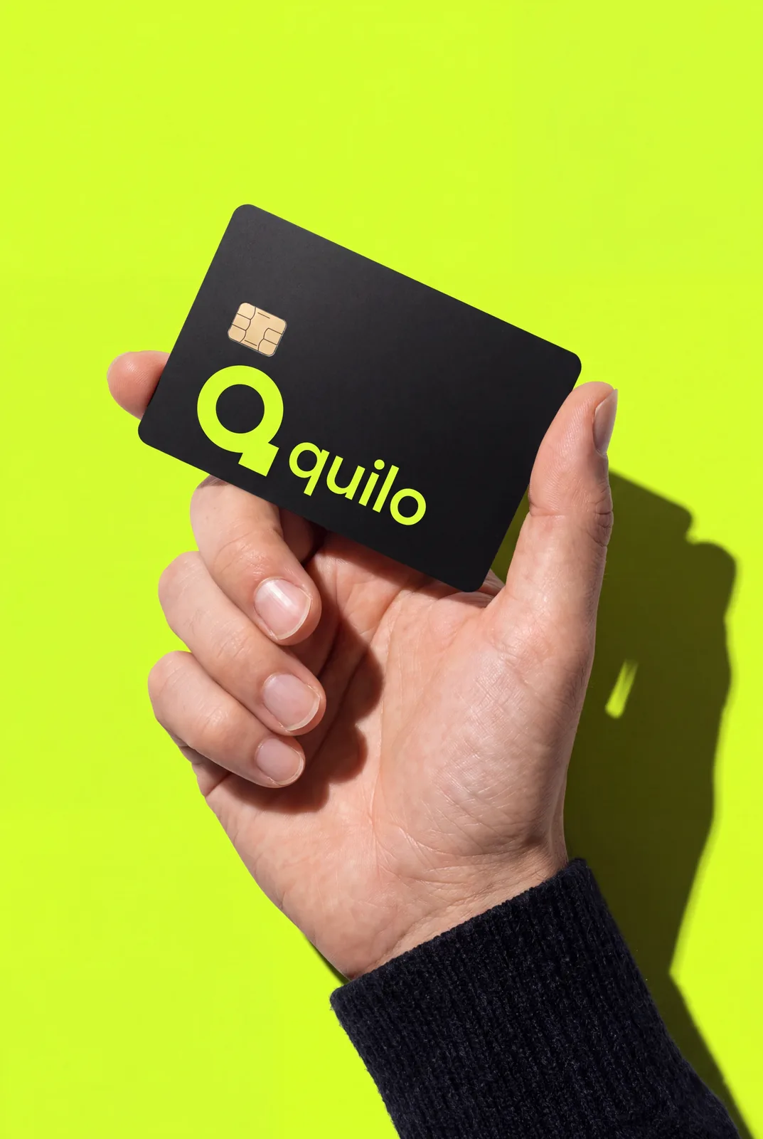 A hand holding a black payment card with a chip and the logo of Quilo, a fictional fintech brand from the Libra branding portfolio