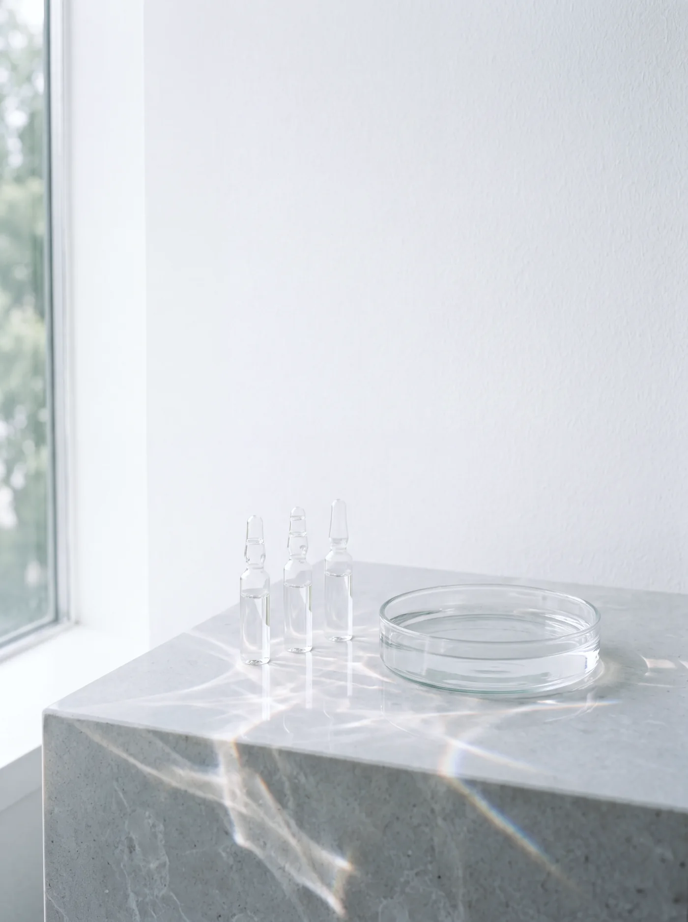Glass ampoules and a dish of water throwing light across stone