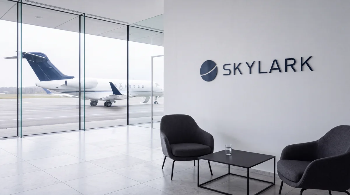 הטרקלין של חברת התעופה הפרטית הבדויה SKYLARK: שתי כורסאות ושולחן נמוך, הלוגו על הקיר, ומטוס מנהלים מאחורי קיר הזכוכית