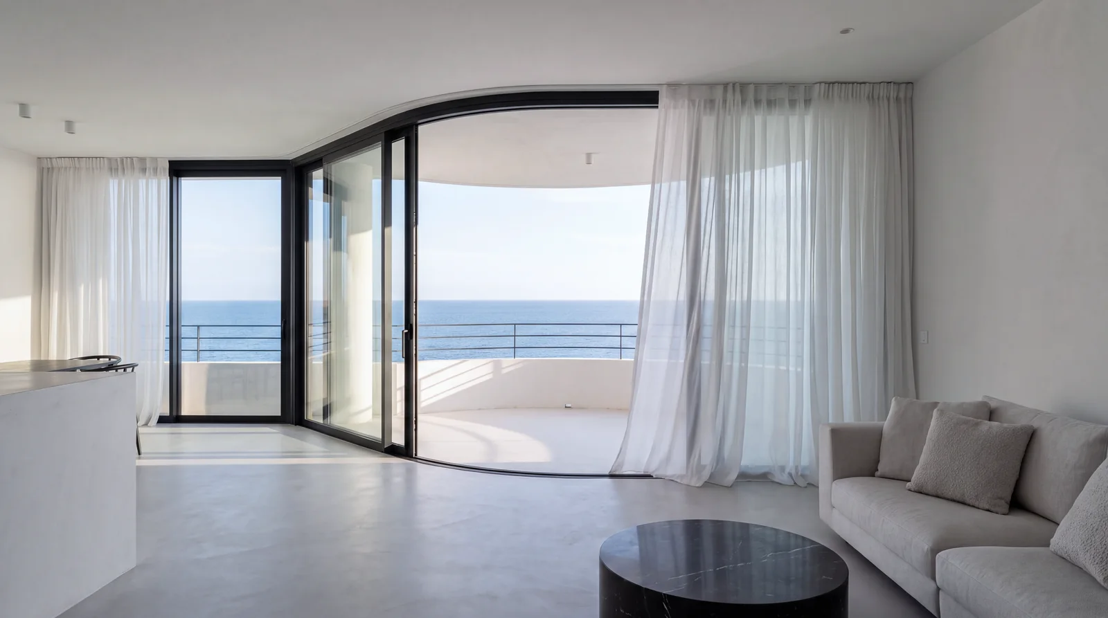 Living room by day with sheer curtains and the sea beyond the balcony